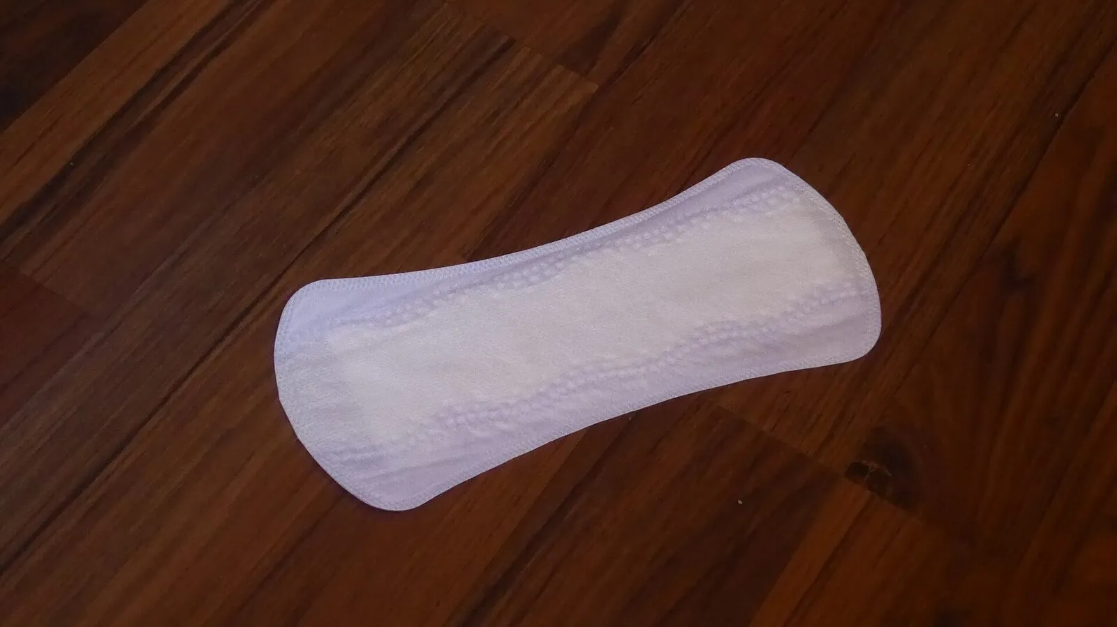 A white disposable sanitary pad with wings, on a wooden table